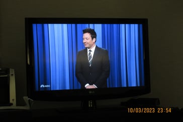 Jimmy Fallon standing in front of a blue curtain 