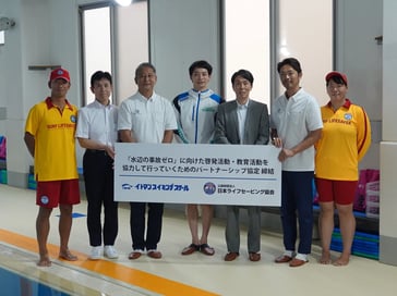 イトマンスイミングスクールと日本ライフセービング協会が『水辺の事故ゼロ』に向けたパートナーシップ協定を締結し、関係者が協定書を持って並んでいる様子