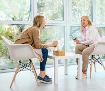 two women sitting at a table with a cup of coffee