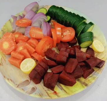 Colorful fresh vegetable salad with sliced cucumber, tomatoes, red onions, carrots, beetroot, and lemon on a plate..