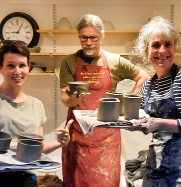 three people standing holding the pots they threw on the beginners course