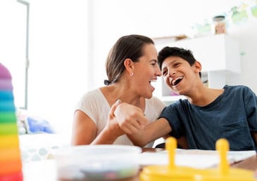 A woman and a boy share a joyful moment, laughing together at a table.