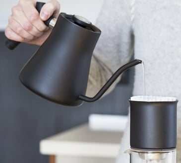 a person pouring water into a cup of coffee