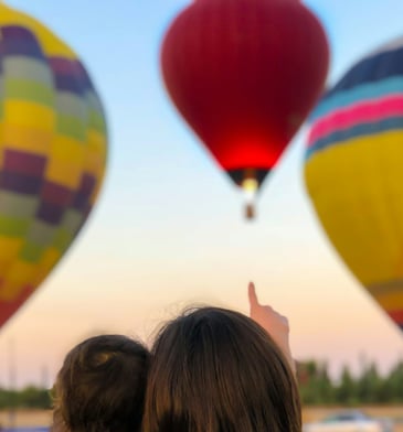 mother holding child pointing at hot air balloon symbolising hope for the future