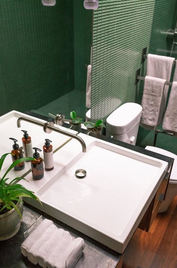 une salle de bain avec plan vasque design, carrelage mosaïque vert, toilettes et sèche serviettes