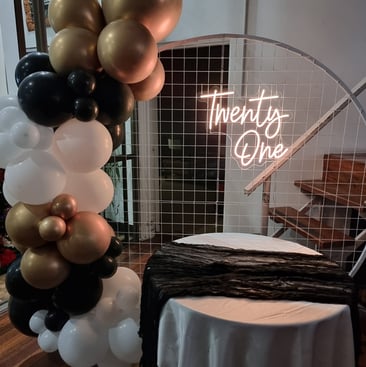 Circle mesh backdrop with a gold Twenty One neon sign with a black, gold and white balloon garland, Redlands.