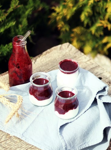 3 pots of yoghurt and berry topping outside with pine trees