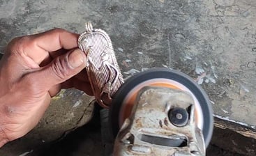 "A tribal artisan carefully filing and refining excess brass from a sculpture after casting in the traditional Dhokra art"