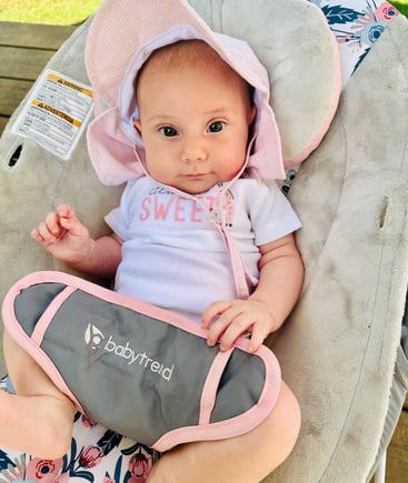 A newborn baby girl with a pink sunhat sitting in a bouncer, looking at the camera