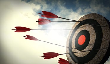 Cork bullseye target with red arrows and cloudy sky background