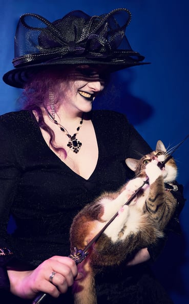 a woman in a black hat holding a cat which is biting a sword
