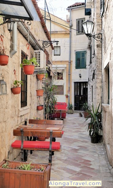 cozy looking red outdoor tables of a restaurant on a narrow cobblestone street of Kotor