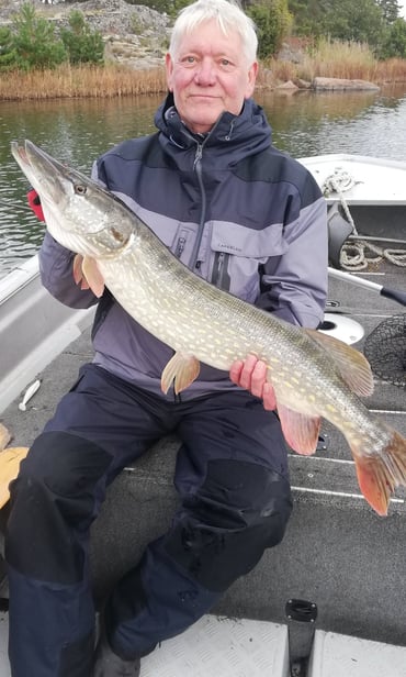 Ein Mann sitzt in einem Fischerboot in Schweden und hält einen schönen Hecht in der Hand.