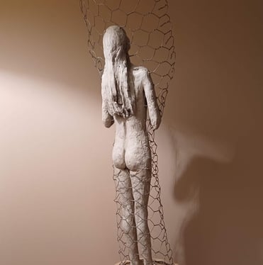 Clay sculpture of a female figure with hands gently placed on chest, surrounded by wire netting.