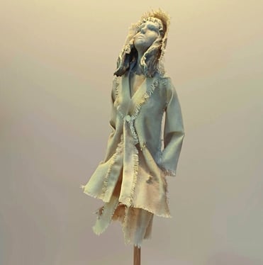 Clay and canvas sculpture of a female figure gazing upwards, wearing windswept, ragged clothes.