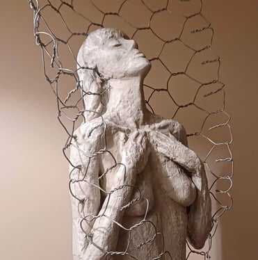 Clay sculpture of a female figure with hands gently placed on chest, surrounded by wire netting.