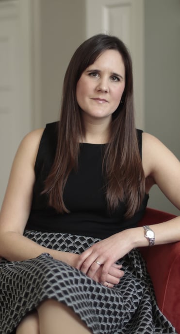 Photo of Anna Joyce CBT for insomnia therapist, sitting in red chair wearing a black geometric dress