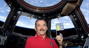 L'astronaute Chris Hatfield, en chemise rouge, tient un drapeau à bord de la Station spatiale