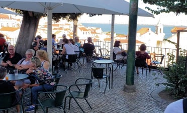 Peopple sitting in outdoor cafe, overlooking Lisbon below as seen from tram 28 wagon.
