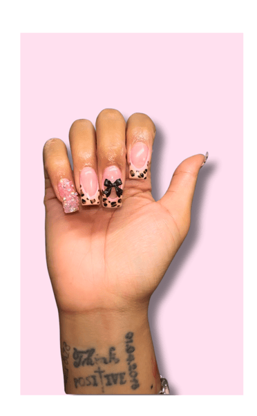 a person's hand with a tattoo on their wrist. Nails are done with a animal print tip and bow accent