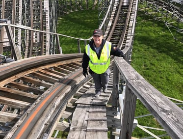 a woman in a safety vest is walking up a wooden roller coaster