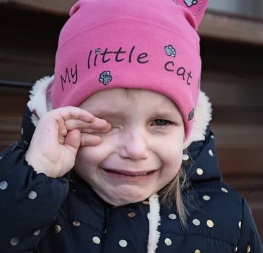 Enfant qui pleure avec bonnet rose (avec inscription My little cat) et doigts main droite sur l'oeil