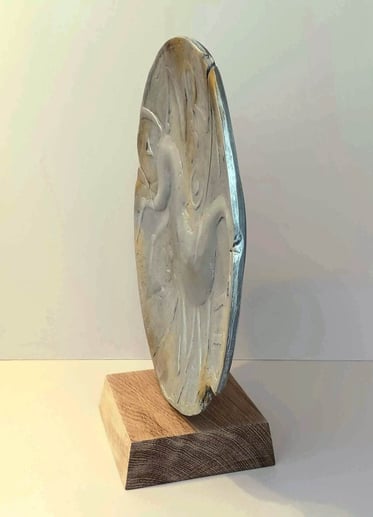 A round plate-like sculpture depicting a stylised horse, painted in blue greys, on oak plinth.