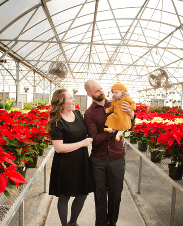 a man and woman holding a baby in a greenhouse