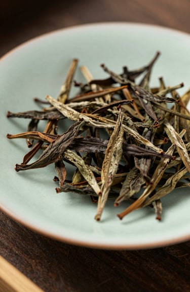 A high-quality close-up of premium dried tea leaves on a handmade East Asian ceramic plate, shot in soft natural light with tea brown and sage green accents.