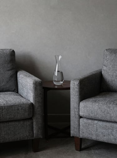 A quiet corner of a mature lounge in Brazil with two comfortable slate grey armchairs and a small side table holding a carafe of water.