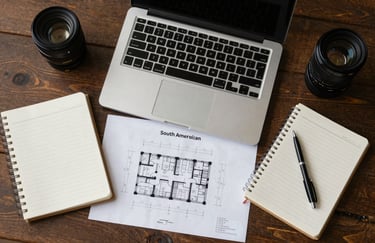A top-down view of a professional desk with a laptop, notebooks, and architectural plans, clean composition, business tools in a South American context.