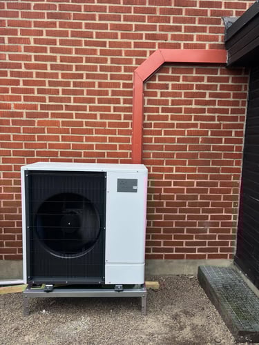 A Mitsubishi Ecodan air source heat pump installed outdoors against a red brick wall.