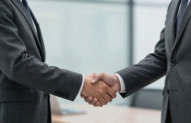 A professional handshake between two individuals in dark charcoal grey business attire, set against a blurred soft blue office background.