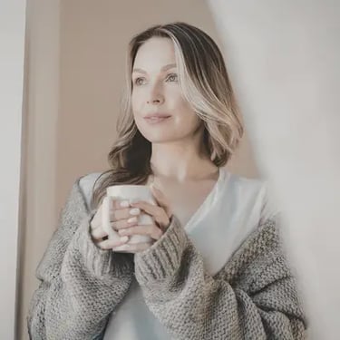 Smiling woman in a cozy oversized grey cardigan holding a coffee mug