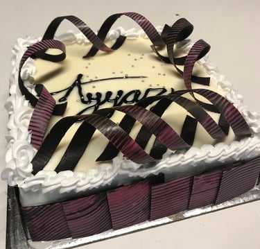 Elegant square white cake with chocolate curls, piped frosting, and silver sprinkles for a celebration.