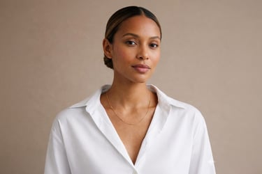 Professional woman with elegant low bun hairstyle wearing a white button-down shirt and gold chain necklace.