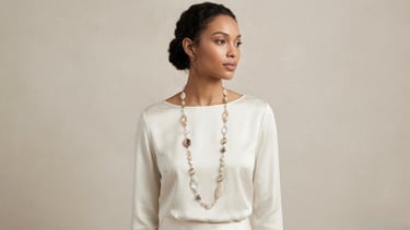 Elegant woman wearing a long beaded statement necklace over a cream silk blouse.