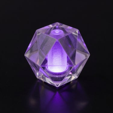 A single geometric translucent 3D printed object glowing with internal violet light on a black mirrored surface.
