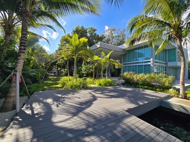 Modern luxury villa with a wooden deck patio surrounded by tropical palm trees.