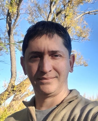 Portrait of a man with short dark hair outdoors against a blue sky and autumn trees.