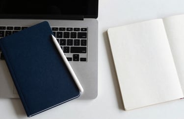 A top-down view of a minimalist desk setup featuring a sleek laptop, a digital stylus, and a notebook in shades of deep midnight blue and bright frost white.