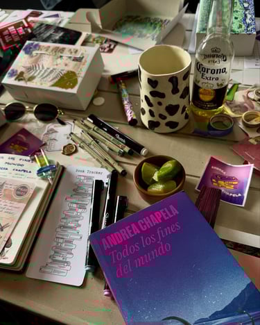 Mesa con artículos de scrappbooking, una bebida y Todos los fines del mundo de Andrea Chapela.