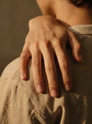 A close-up of a supportive hand resting on a friend's shoulder, bathed in warm golden light.