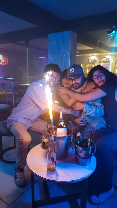 Friends celebrating at a nightclub with bottle service, sparklers, and drinks at a VIP table.