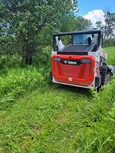 Red Bobcat skid steer parked in tall grass used for land clearing in Oshawa