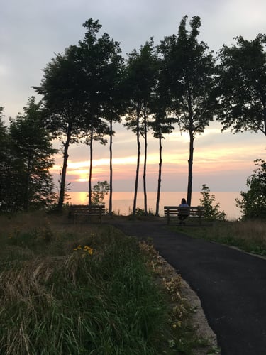 A woman sitting at a bench overlooking a lake at sunset.