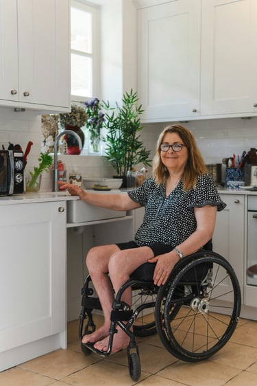 A smiling woman in a wheelchair using an accessible white modern kitchen with low counters.