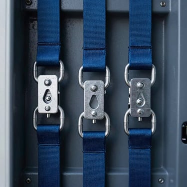 Close-up of professional cargo securing equipment inside a modern transport vehicle, focusing on the heavy-duty straps and metallic hooks, steel blue tones. Central European / Swiss German.