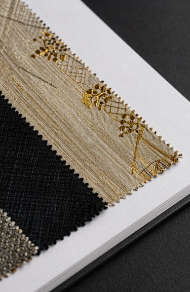 Detail of a luxury textile swatch book showing various textures in black, gold, and off-white.