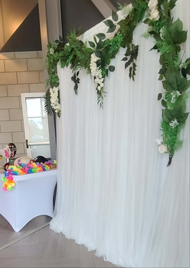 Elegant white draped backdrop with floral greenery garland for a wedding or event photo booth.